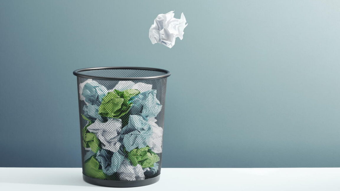 A crumpled ball of paper flies toward a overflowing trash can